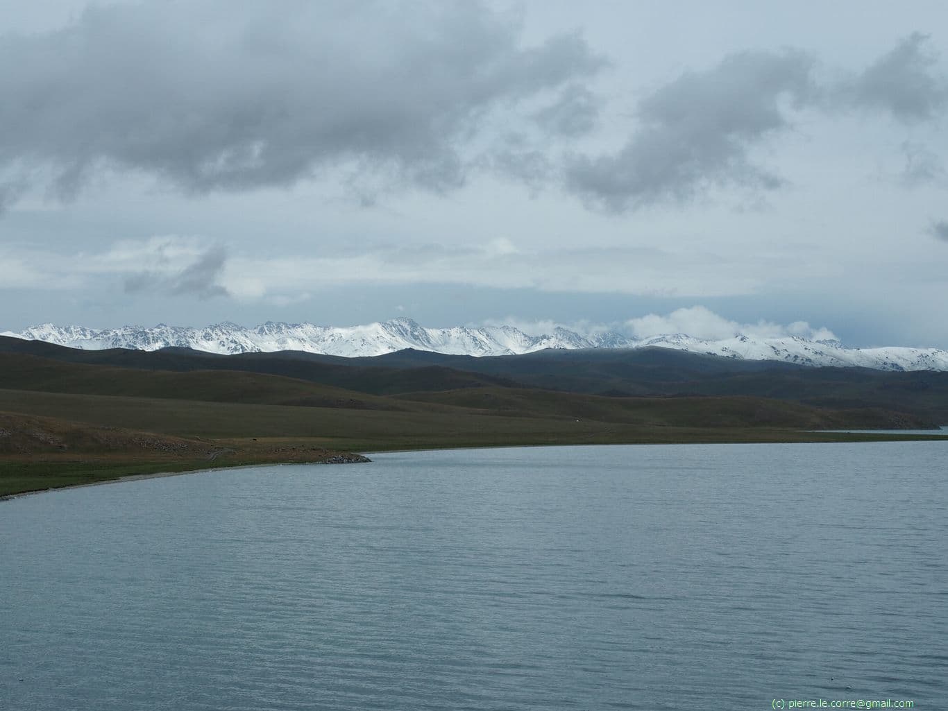 Vue en hauteur sur le lac Song Kul et une chaîne montagneuse enneigée au loin